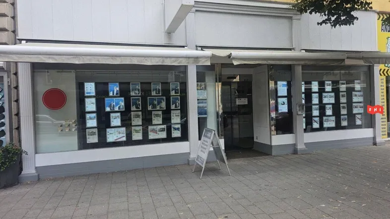 Immobilienbüro mit großen Schaufenstern voller Angebote an einer belebten städtischen Straße.
