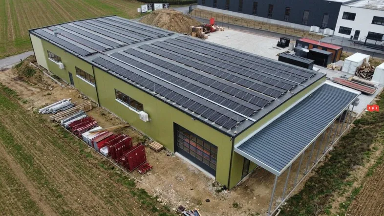 Luftaufnahme eines modernen Gewerbegebäudes mit Photovoltaikanlage auf dem Dach und umliegendem Gelände.