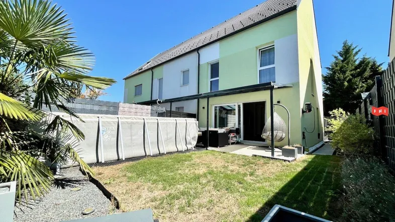 Hinterhof mit Rasenfläche, aufgestelltem Pool und überdachter Terrasse, umgeben von Grün.