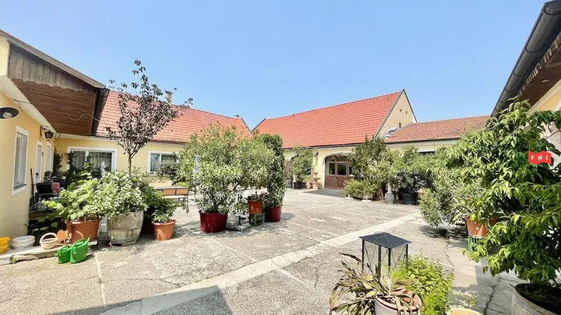 Großer Innenhof mit vielen Pflanzen und gepflastertem Boden, umgeben von Gebäuden mit roten Ziegeldächern.