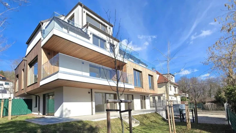 Modernes Mehrfamilienhaus mit Holzfassade und großen Balkonen unter blauem Himmel.