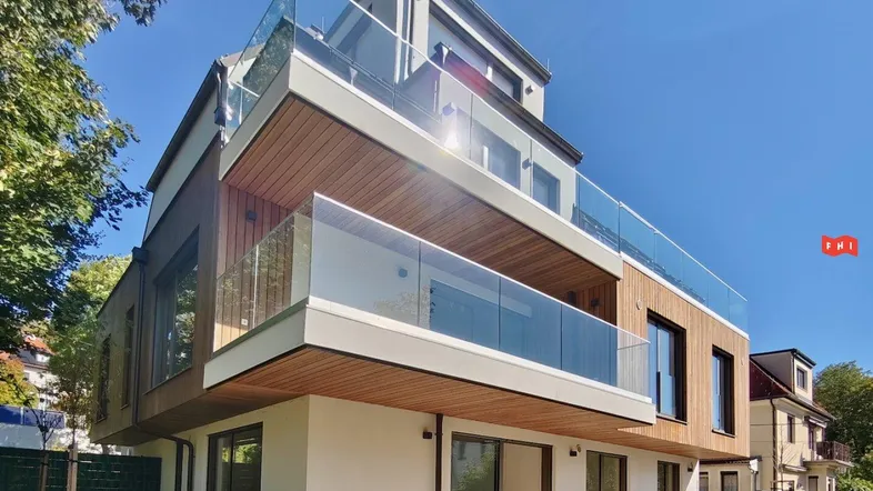 Modernes Mehrfamilienhaus mit Holzfassade, großen Glasfronten und Balkonen mit Glasgeländer.
