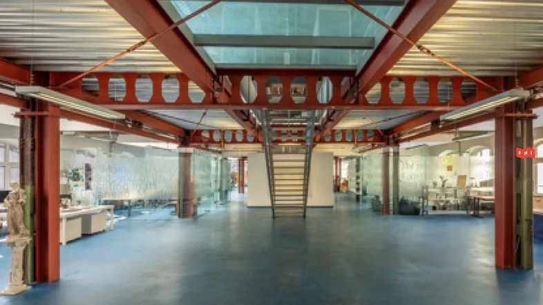 Großes, offenes Büro mit industriellem Design, roten Stahlträgern, Glaswänden und zentraler Treppe.