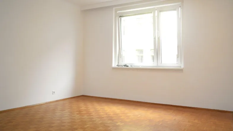 Helles Zimmer mit Parkettboden und großem Fenster, bereit zur individuellen Gestaltung.