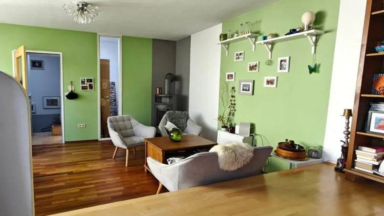 Gemütliches Wohnzimmer mit grünen Wänden, Holzboden und bequemen Sitzgelegenheiten.