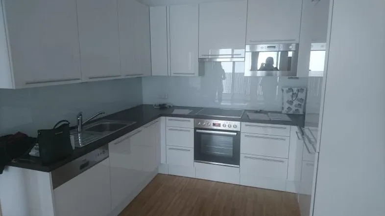 Moderne Einbauküche in Weiß mit glänzenden Fronten, integrierten Geräten und Holzboden.