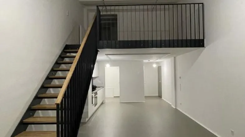 Geräumiger, offener Wohnbereich mit hohen Decken, moderner Treppe und Mezzanine-Ebene.