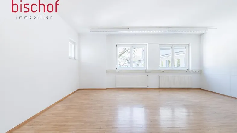 Heller, leerer Raum mit großen Fenstern und Holzboden, ideal für Büronutzung oder als Arbeitszimmer.