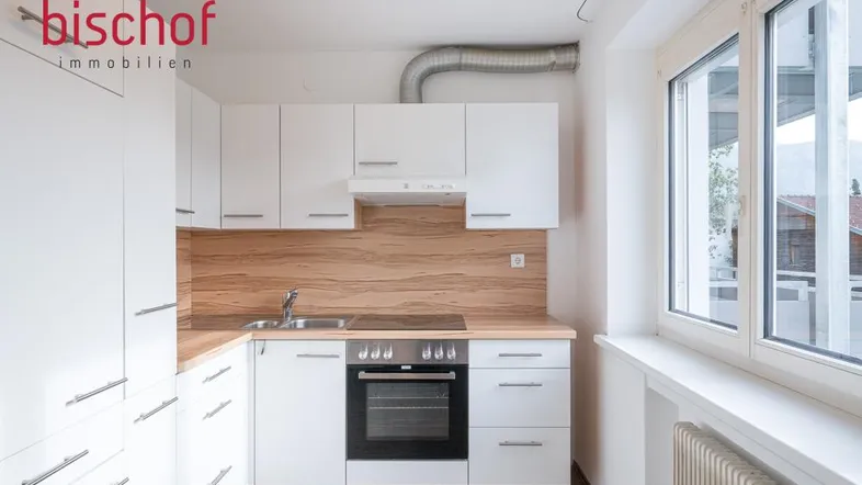 Helle Einbauküche mit weißen Schränken, Holzoptik-Arbeitsplatte und Blick ins Grüne.