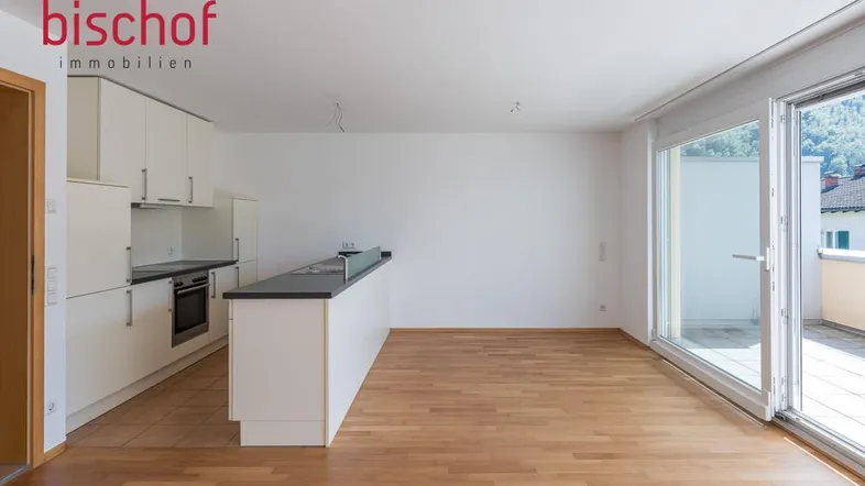 Heller offener Wohn-Essbereich mit integrierter Küche, Parkettboden und Zugang zum Balkon.