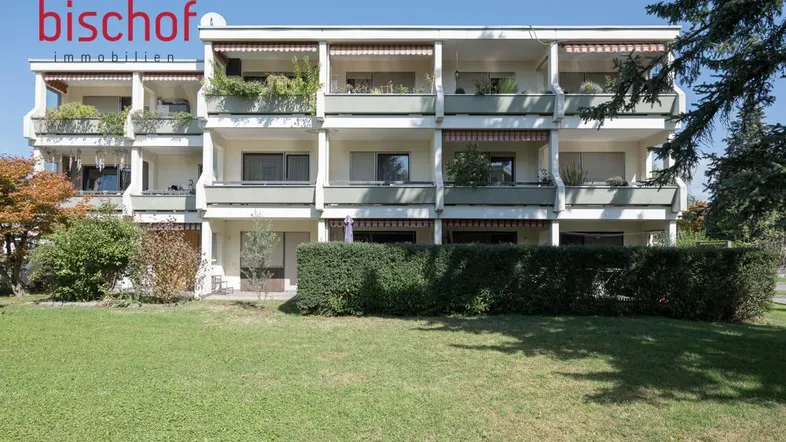 Mehrfamilienhaus mit mehreren Balkonen und gepflegter Grünanlage im Vordergrund.