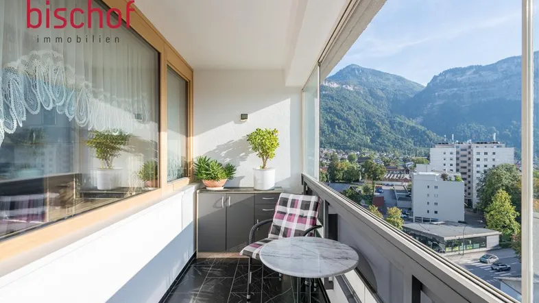 Heller Balkon mit Sitzgelegenheiten, Pflanzen und einem weiten Blick auf die Berge und die Stadt.