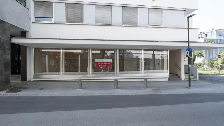 Gebäudefassade mit großen Schaufenstern und einem 'zu vermieten'-Schild, das auf die Verfügbarkeit hinweist.