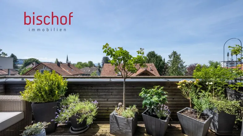 Dachterrasse mit Holzboden, vielen Pflanzen und Blick über die Dächer der Umgebung.