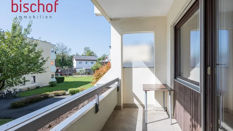 Heller Balkon mit Blick auf den grünen Innenhof und umliegende Gebäude.
