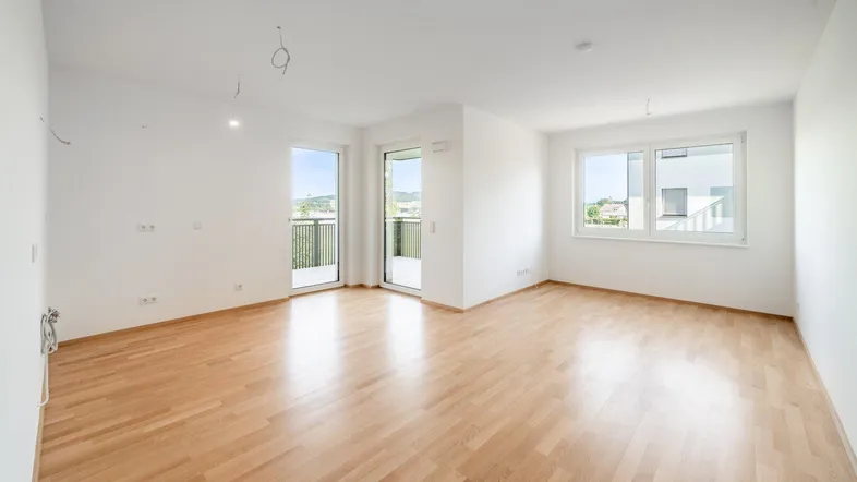 Helles, leeres Zimmer mit Parkettboden und Zugang zu einem Balkon, bietet viel natürliches Licht.