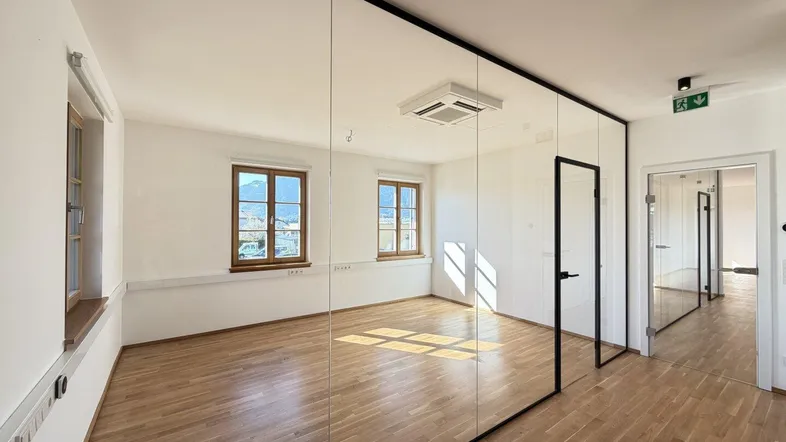 Heller Büroraum mit modernen Glaswänden, Holzboden und Blick auf die umliegende Landschaft.