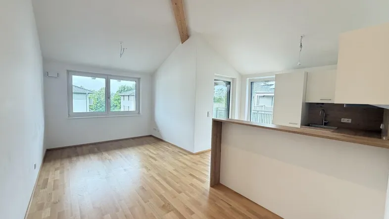 Heller Wohn- und Kochbereich mit Holzbalken, Parkettboden und Dachschräge in einem Neubau.