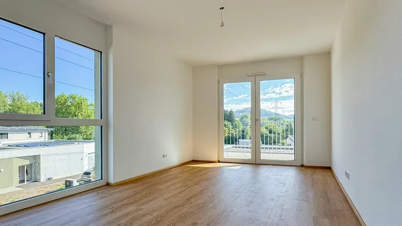 Heller Wohnraum mit großen Fenstern, Laminatboden und Zugang zu einem Balkon mit Weitblick.