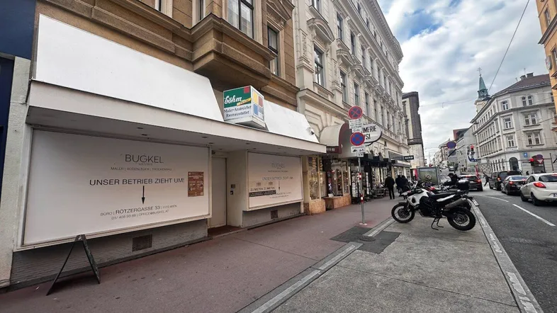 Straßenansicht eines Geschäftsgebäudes mit Schaufenstern und darüber liegenden Wohnungen in urbaner Umgebung.