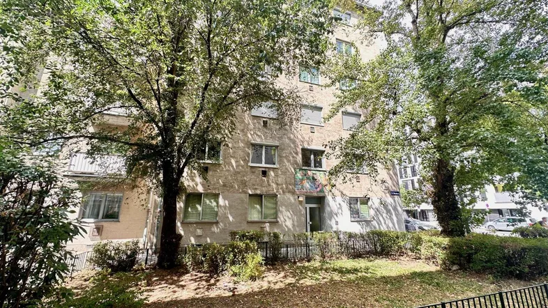 Gepflegte Gebäudefassade eines Mehrfamilienhauses, umgeben von altem Baumbestand und Grünflächen.