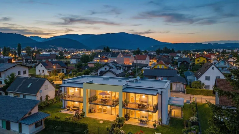 Moderne Wohnanlage bei Sonnenuntergang mit beleuchteten Balkonen und Bergblick.