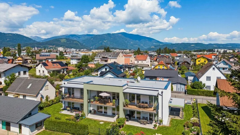 Moderne Wohnanlage mit Balkonen und Terrassen, umgeben von Grünflächen und Bergblick.