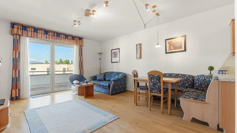Helles Wohn- und Esszimmer mit Holzboden, gemütlicher Sitzecke und Zugang zum Balkon.