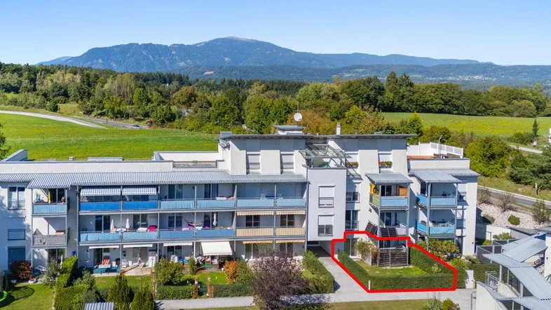 Luftaufnahme eines Mehrfamilienhauses mit eigenem Gartenbereich und malerischem Bergblick.