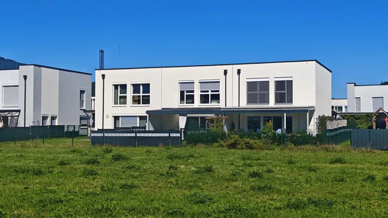 Moderne Reihenhäuser mit weißer Fassade und großen Fenstern, umgeben von Grünflächen.