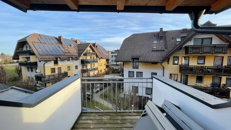 Balkon mit Holzboden und Blick auf umliegende Gebäude, einige davon mit Photovoltaikanlagen ausgestattet.