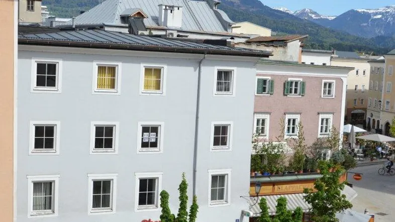 Blick von oben auf eine belebte Straße mit Geschäften, Gebäuden und Bergen im Hintergrund.