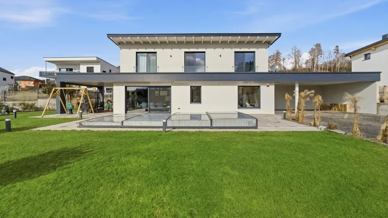 Modernes Einfamilienhaus mit großem Garten, Rasenfläche und Kinderschaukel unter blauem Himmel.