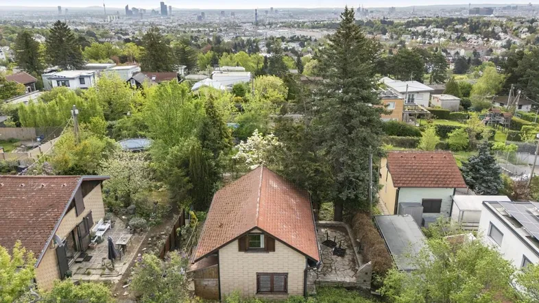 Luftaufnahme eines Hauses mit rotem Dach und Blick auf die Stadt Wien im Hintergrund.
