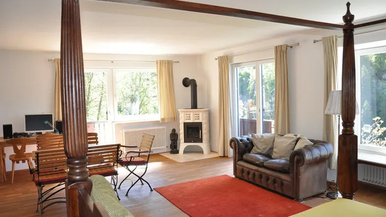 Geräumiges Wohnzimmer mit Kaminofen, Holzboden und Zugang zu einem Balkon mit Blick ins Grüne.
