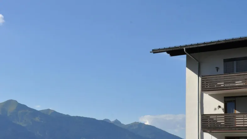 Gebäude mit Balkonen und beeindruckendem Bergblick in einer grünen alpinen Landschaft.