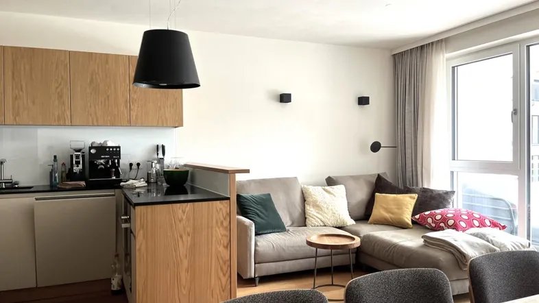 Moderne offene Küche mit Holzelementen und angrenzendem Wohnbereich mit Sofa.