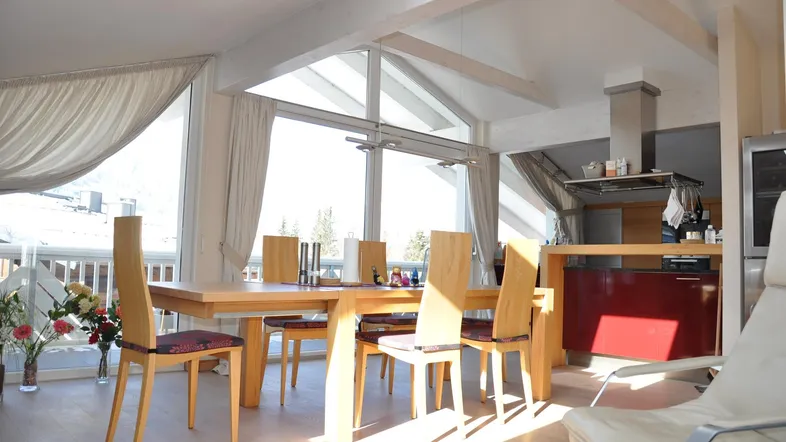 Heller Essbereich mit Holztisch, großen Fenstern, Zugang zum Balkon und Blick auf die verschneite Landschaft.