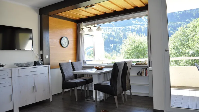 Heller Wohn- und Essbereich mit Bergblick, Holzakzenten und Zugang zum Balkon.
