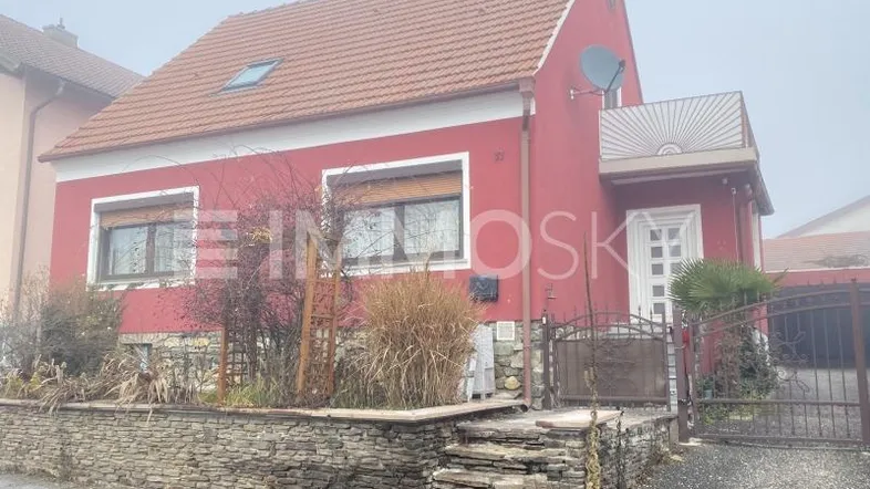 Rotes Einfamilienhaus mit Satteldach, Rollläden und einem kleinen Vorgarten.