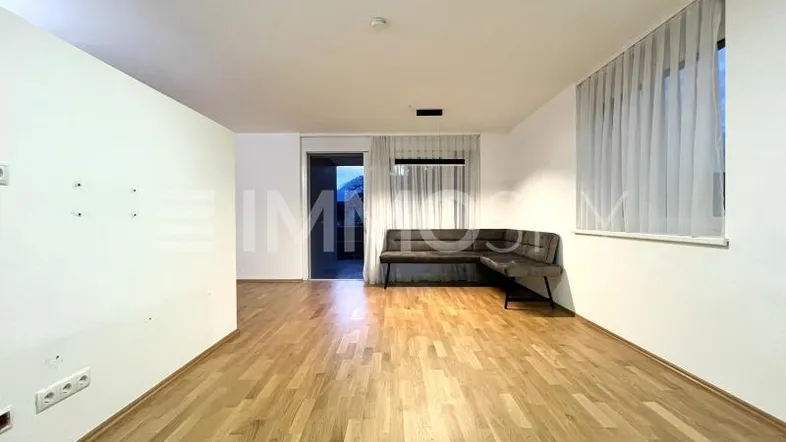Geräumiges Wohnzimmer mit hellem Parkettboden, weißen Wänden und einem gemütlichen Ecksofa.