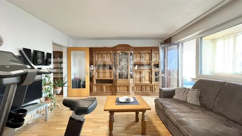 Geräumiges Wohnzimmer mit Holzboden, gemütlichem Sofa und Zugang zu einem verglasten Balkon.