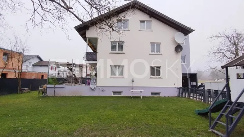 Mehrfamilienhaus mit Garten, Rasenfläche und kleinem Spielplatz im Außenbereich.