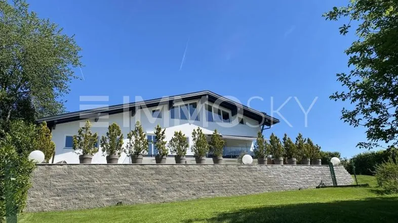 Modernes Haus mit weißer Fassade, großen Fenstern und gepflegtem Gartenbereich unter blauem Himmel.