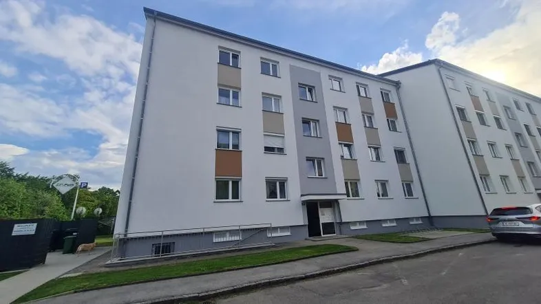 Modernes Mehrfamilienhaus mit weißer Fassade und grauen Akzenten unter bewölktem Himmel.