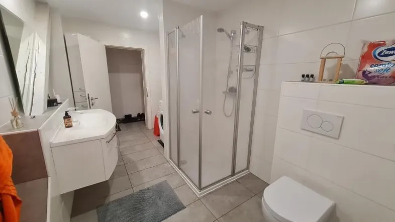 Modernes Badezimmer mit Duschkabine, Waschbecken und Toilette, hell gefliest.