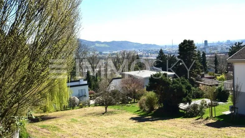 Weitläufiges Grundstück mit grüner Wiese und Fernblick auf die Stadt und Berge.