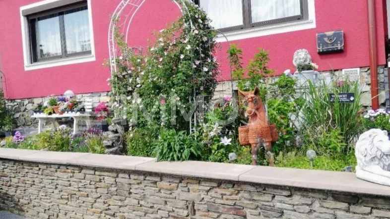 Vorgarten mit Steinmauer, blühenden Pflanzen und dekorativen Elementen vor dem Haus.