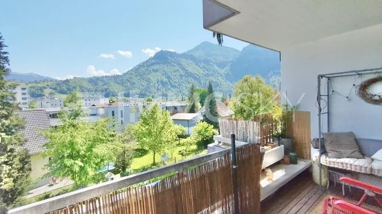 Sonniger Balkon mit Holzboden, Sitzgelegenheiten und weitem Bergblick.