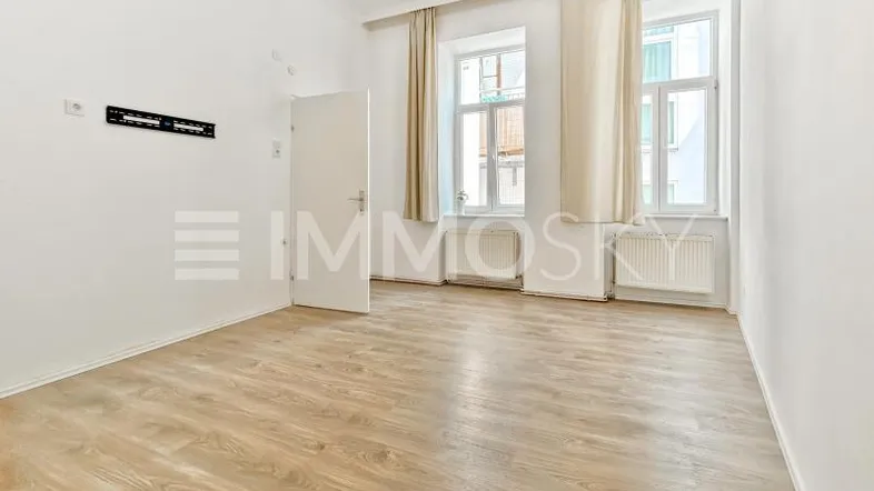 Helles Zimmer mit Laminatboden, weißen Wänden und zwei Fenstern, bereit zur Einrichtung.